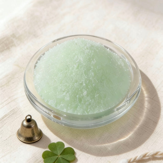 Light green candle wax granules in a glass bowl, styled with a four-leaf clover, brass bell and twine