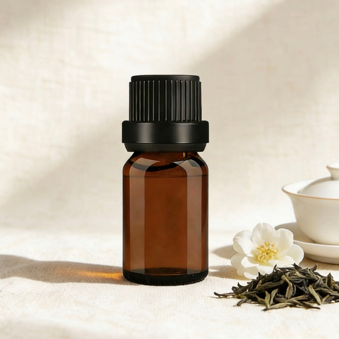 Amber glass bottle of white tea-scented essential oil, surrounded by delicate jasmine flowers and loose tea leaves, ideal for creating calming, fresh aromatherapy blends, white tea-scented candles, and natural wellness products