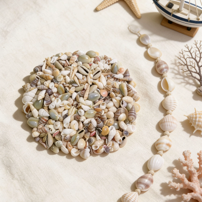 Assorted seashells arranged in a circular pile, surrounded by nautical decor including a seashell garland, starfish, model sailboat, and coral, ideal for candle making and beach-themed crafts