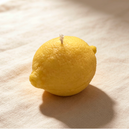 Bright yellow lemon-shaped candle with realistic peel texture on a linen background
