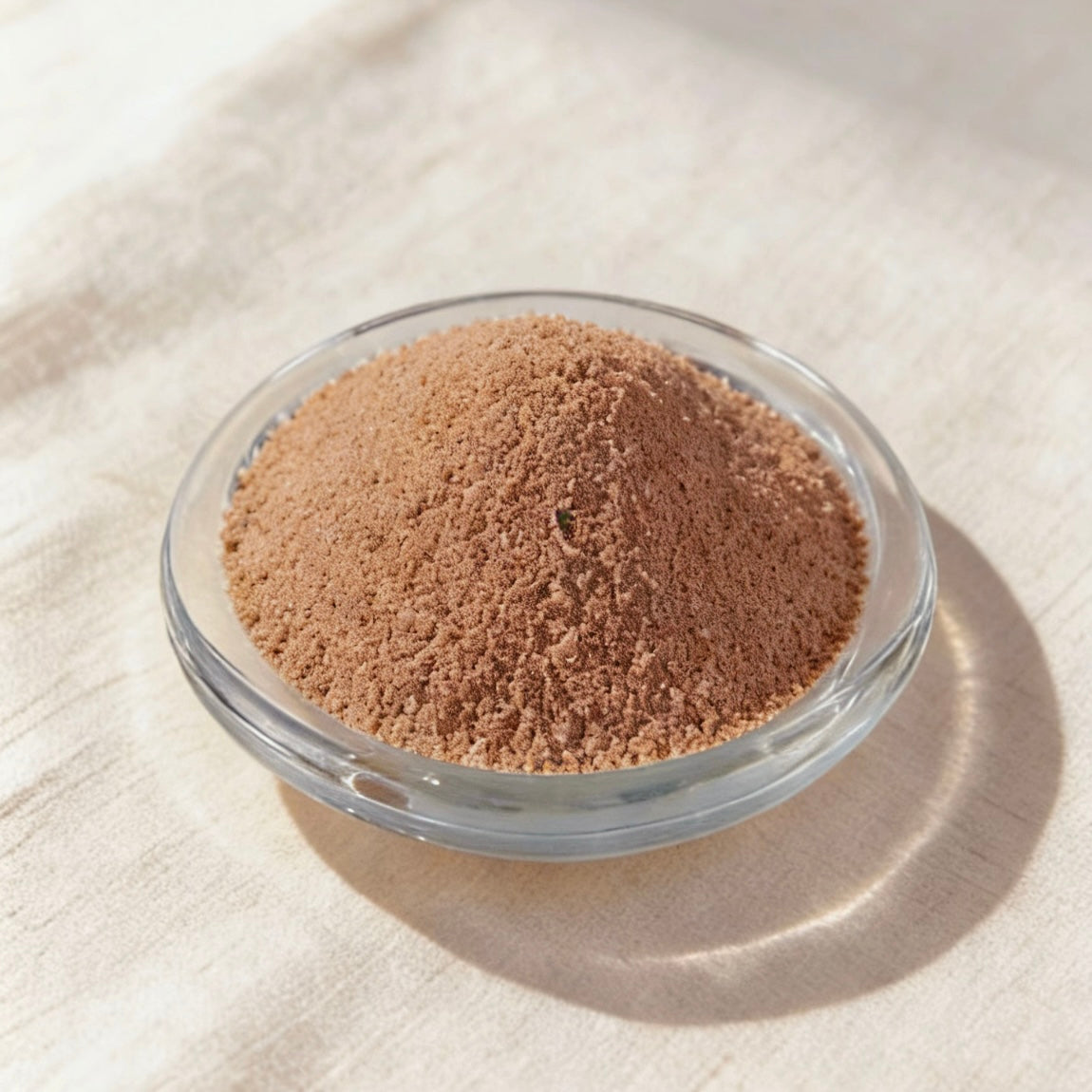 Brown candle wax powder in a clear glass bowl on a white linen background
