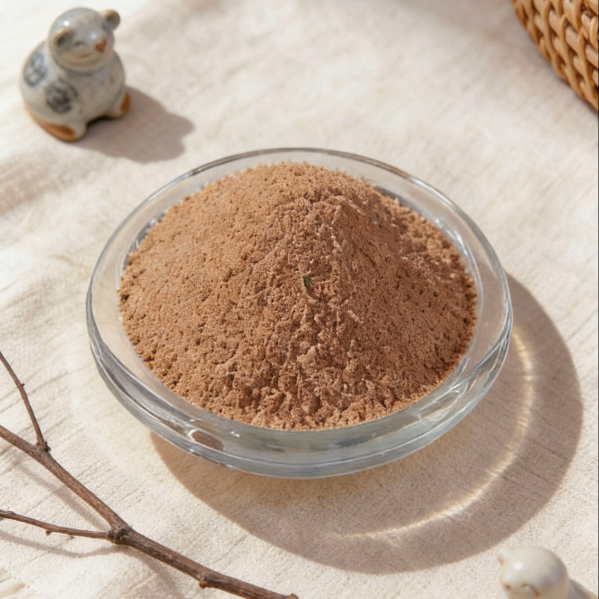 Brown candle wax powder in a glass bowl, styled with ceramic animal figurines and a dry branch on a linen surface
