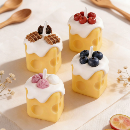 Assortment of realistic cheese-shaped candles with white cream wax drizzle, topped with decorative waffle, cookie, cherry, blueberry, and ice cream wax sculptures, styled with wooden utensils, dried flowers, and citrus slices on a neutral background
