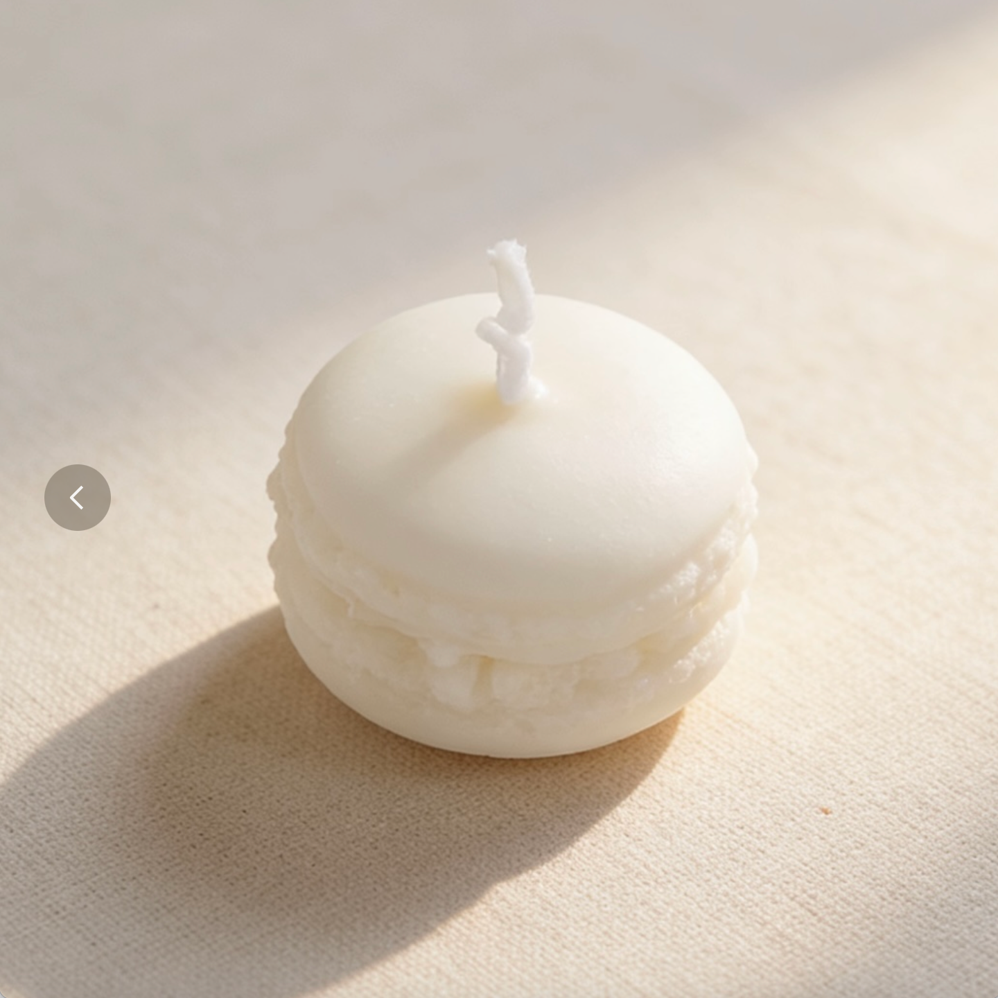 Creamy white macaron-shaped candle with textured filling on a neutral linen background