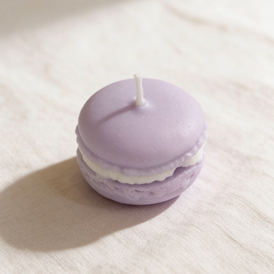 Lavender macaron-shaped candle with white cream filling on a soft linen surface