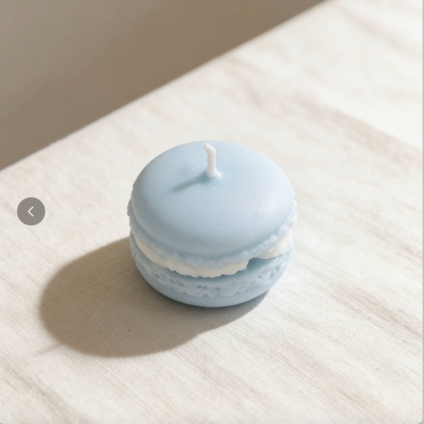 Light blue macaron-shaped candle with white filling on a neutral linen background
