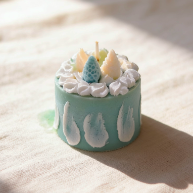 Light blue mini cake-shaped candle with whipped cream and fruit toppings