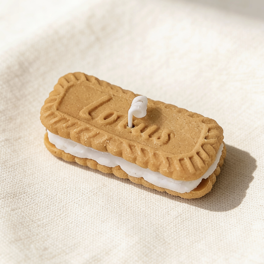 Realistic sandwich cookie-shaped candle, styled after Lotus Biscoff biscuits, with golden-brown embossed cookie layers, white cream filling, and an embossed "Lotus" logo, featuring a cotton wick, displayed on a neutral background