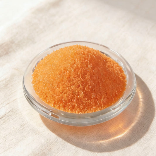 Vibrant orange candle wax granules in a clear glass bowl on a soft linen background
