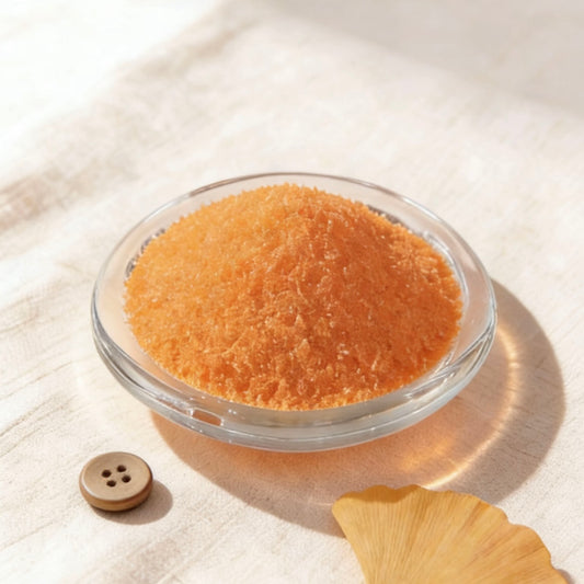 Orange candle wax granules in a glass bowl, styled with a ginkgo leaf, twine and wooden button
