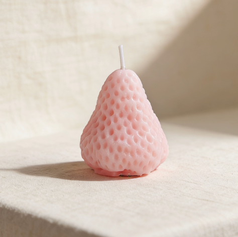 Pastel pink strawberry-shaped candle on a linen background