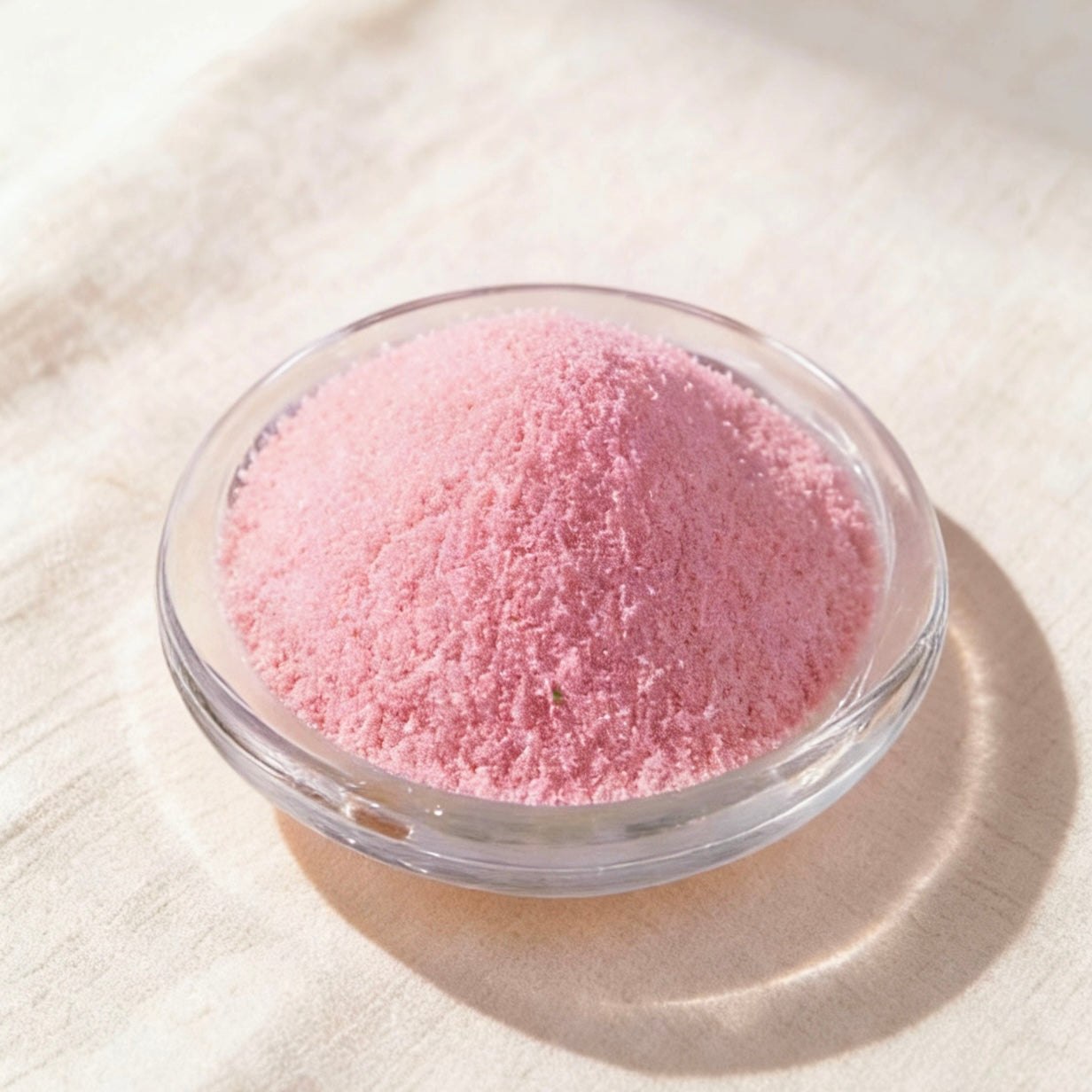 Soft pink candle wax powder in a clear glass bowl on a white linen background