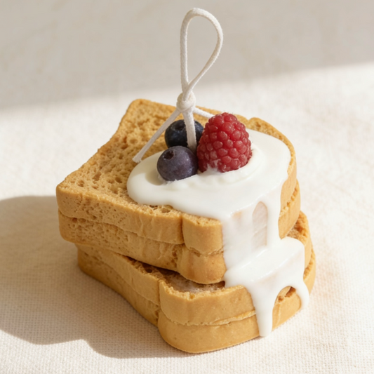 Realistic stacked toast-shaped candle with white cream wax dripping down the sides, topped with decorative blueberry and raspberry wax sculptures, with a cotton wick, displayed on a neutral background
