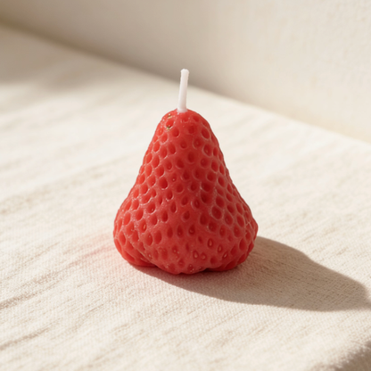 Vibrant red strawberry-shaped candle on a neutral linen surface
